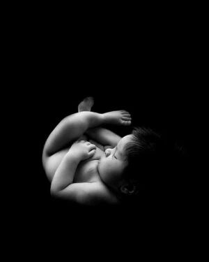Peacefully sleeping baby on smooth black posing tool 'Create-a-Nest' for newborn photography