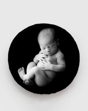 Naked newborn baby posed on soft black poser 'Create-a-Nest' during a photo session