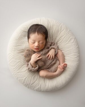 Baby in a soft ivory poser cover styled with neutral newborn photography props