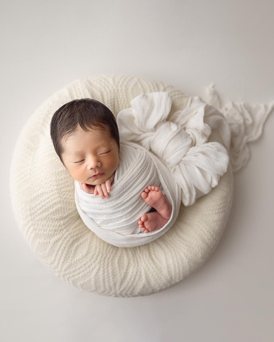 Newborn baby posed on the ivory Create‑a‑Nest™ poser cover from the Gordon collection