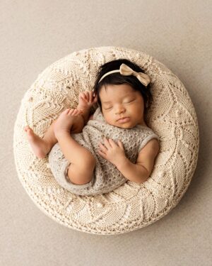 Full‑body shot of newborn girl posed in a romper on the ranch‑tan posing prop for photography