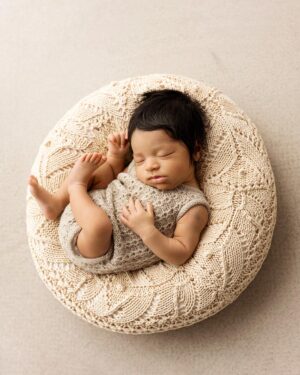 Newborn boy in a romper posed on the ranch‑tan bean bag poser Perry during a photo session