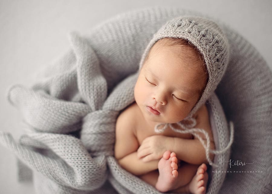 Close-up of a newborn baby on a grey poser setup, styled with soft neutrals.