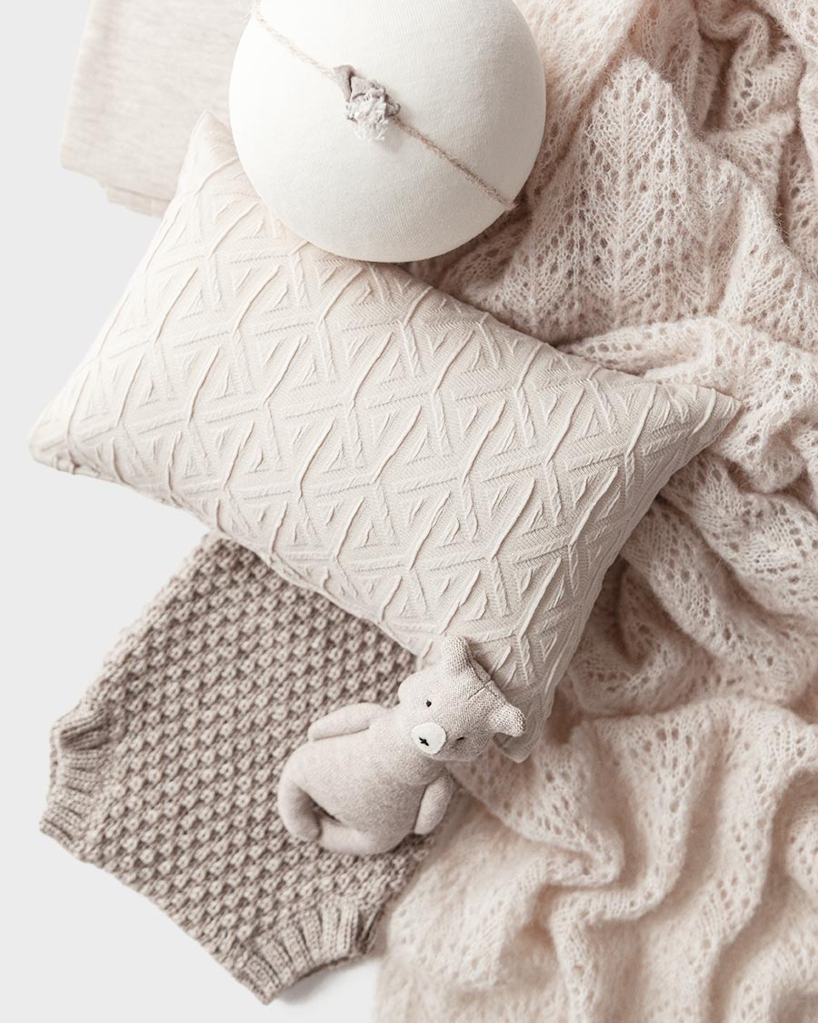 Close‑up of coordinated oatmeal baby photography props including a textured wrap, stretchy backdrop, knit shorts, matching pillow, delicate headband, and cuddly teddy bear – ideal for a newborn picture.