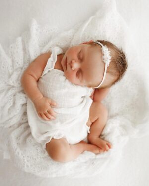 Baby girl posed on cream‑coloured pointelle wrap used as a textured layer for newborn photo shoot