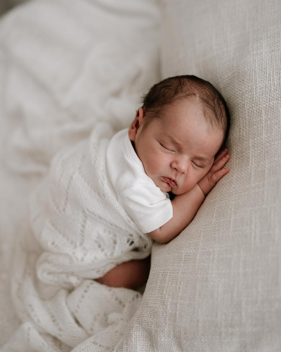 Baby gently covered with a knitted pointelle wrap in a soft newborn photography setup.